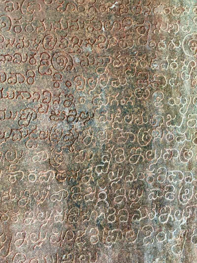 A close view of a reddish stone surface shows about fifteen lines of rounded, engraved letters.