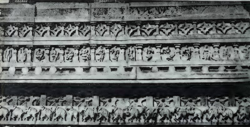 A carved stone wall in horizontal bands of star-shaped motifs and small statues, with a row of elephants along the bottom.