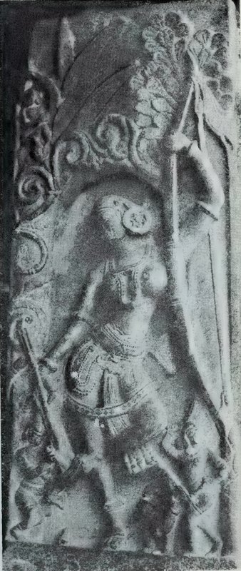 A carved woman holding a long bow or staff under a carved tree, with small statues at her feet.