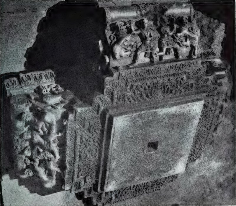A large carved stone capital seen from below, with a plain square face, carved borders and statues along its upper edge.
