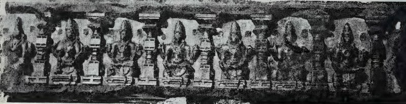 A long, weathered carved panel with a row of seated statues between small pillars.