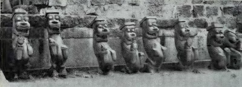 A row of weathered stone lion brackets standing in front of a masonry wall.