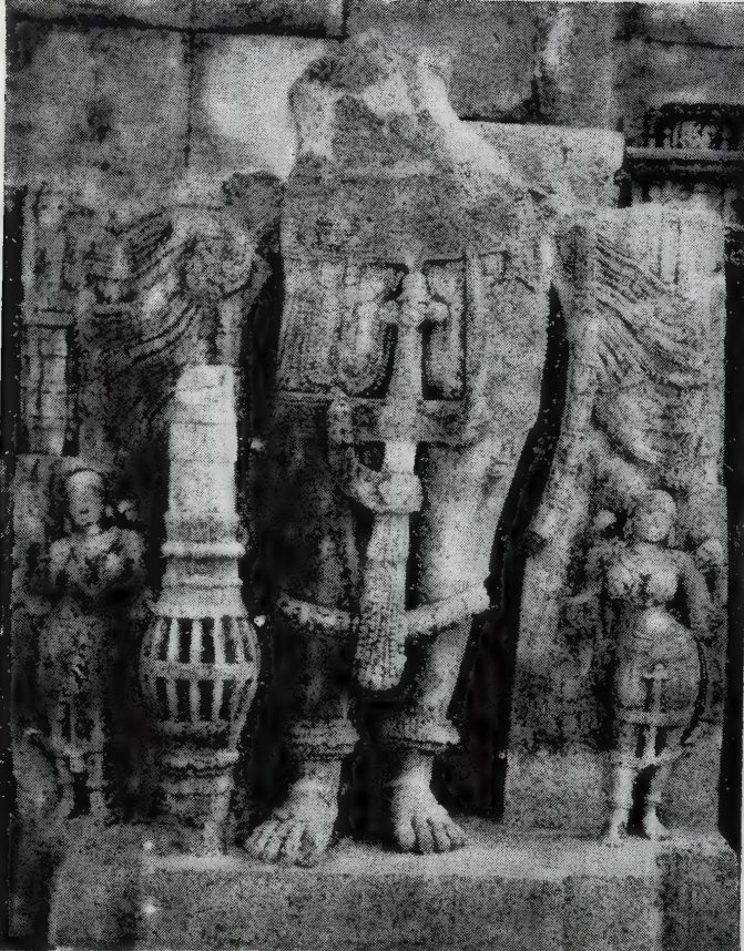 The lower part of a broken standing statue, showing its legs and feet, a ribbed mace and small attendant statues on either side.