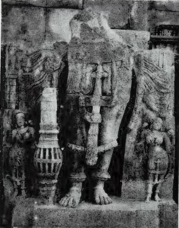 The lower part of a broken standing statue, showing its legs and feet, a ribbed club-like object and small attendant statues.