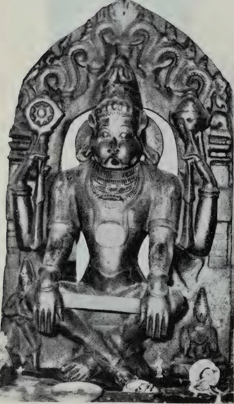A seated four-armed god with a lion face, holding a discus and a conch in the upper hands, under an ornate carved arch.