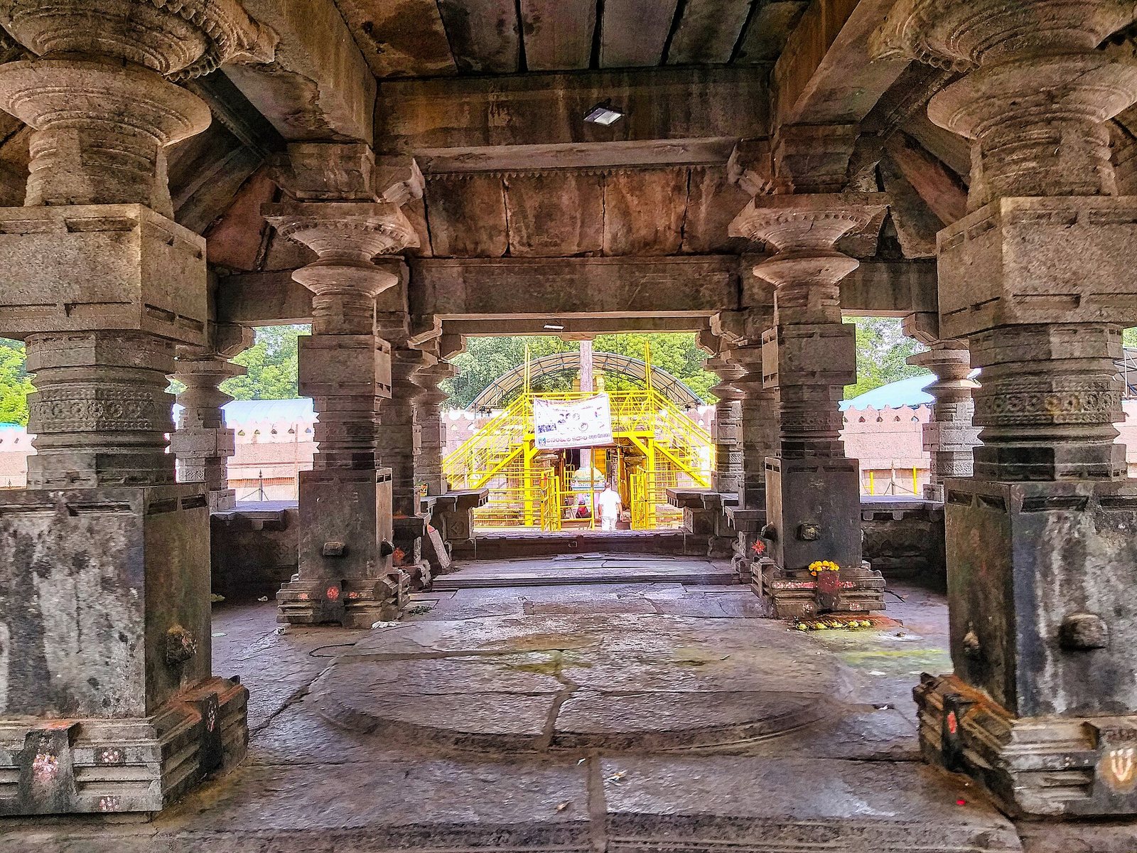 Inside a dim stone hall, heavy turned pillars stand on square bases around a round stone platform in the centre of the floor.