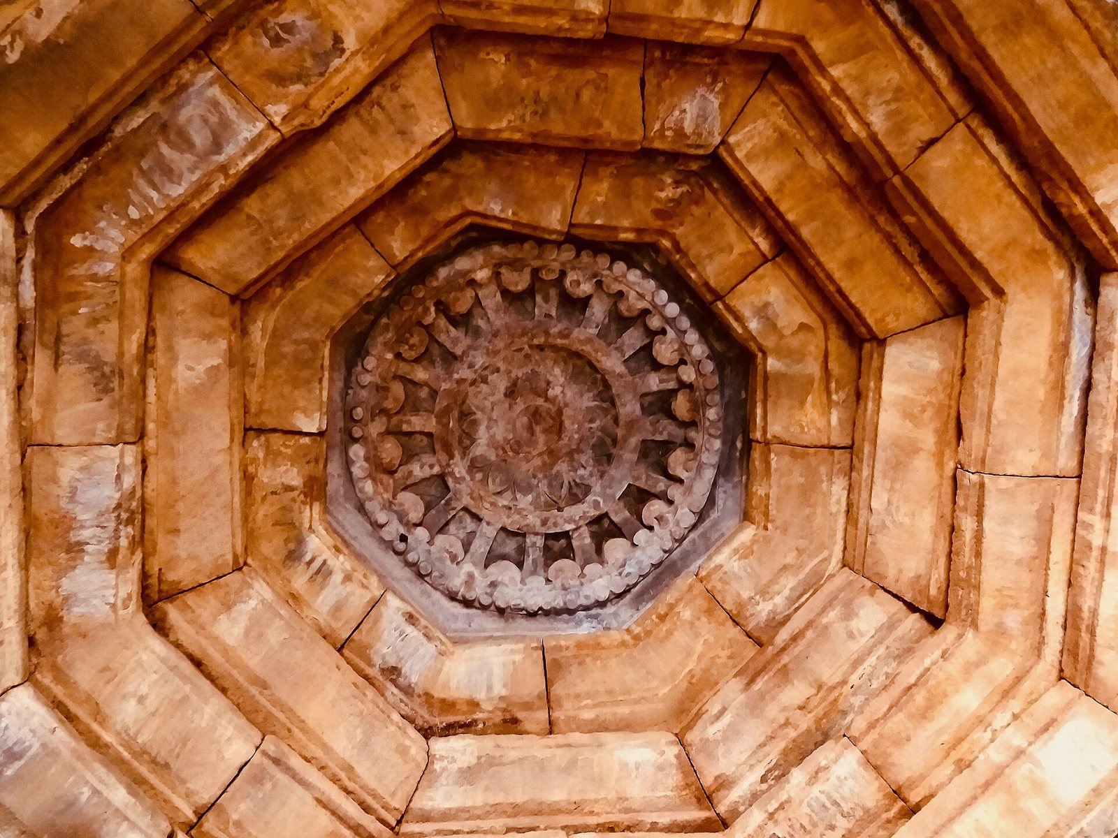 Looking straight up at a stone ceiling made of stepped octagonal frames, with a round carved lotus at the centre.