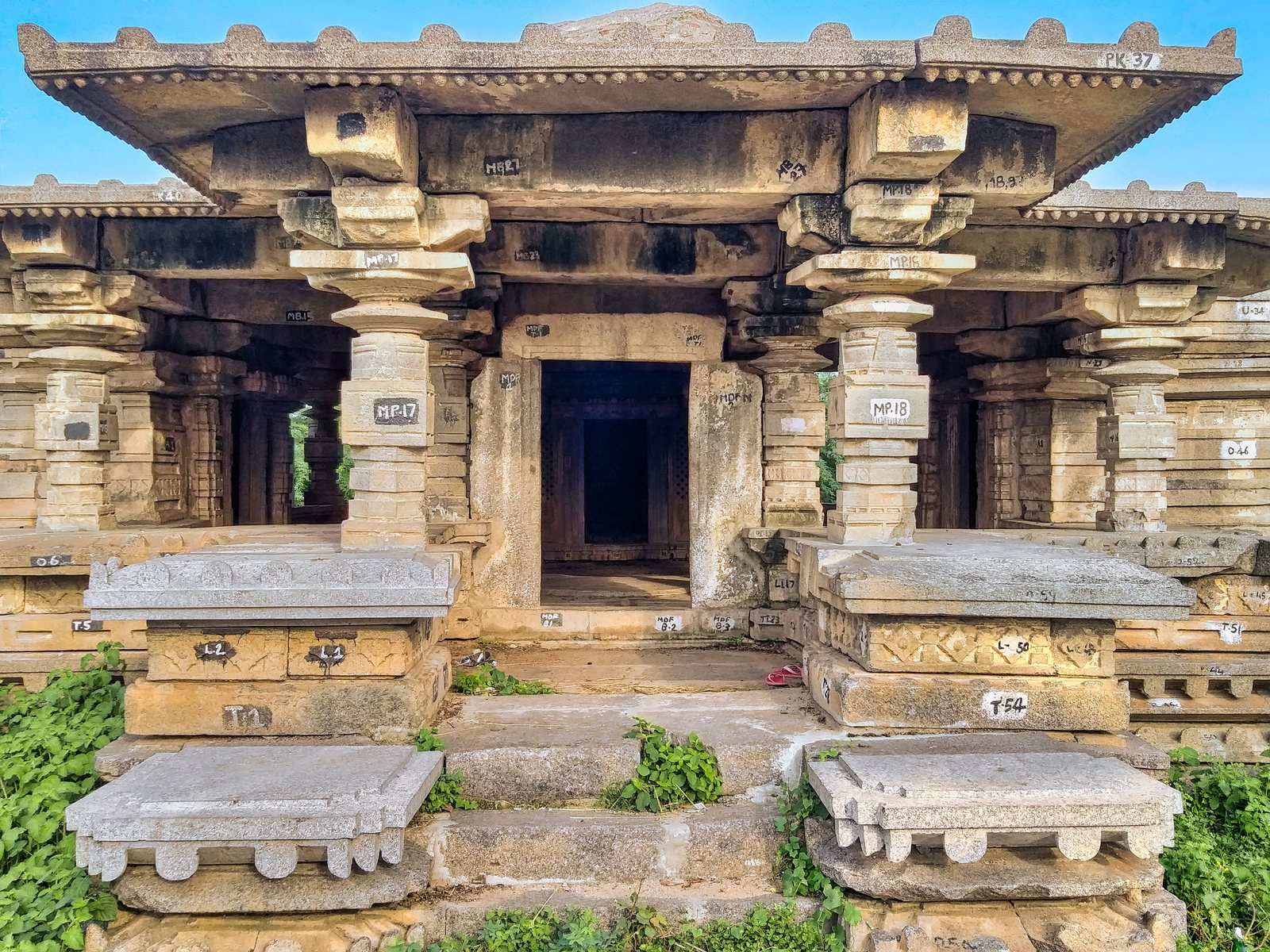 A pillared stone hall with a flat roof and wide eaves stands on a platform. Steps lead to a central doorway, and many stones carry painted numbers.