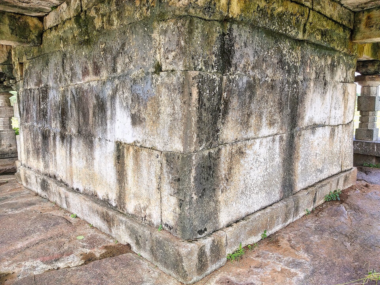 A corner of a plain wall of large, weathered stone blocks stands on a low base, under the ceiling of the hall.