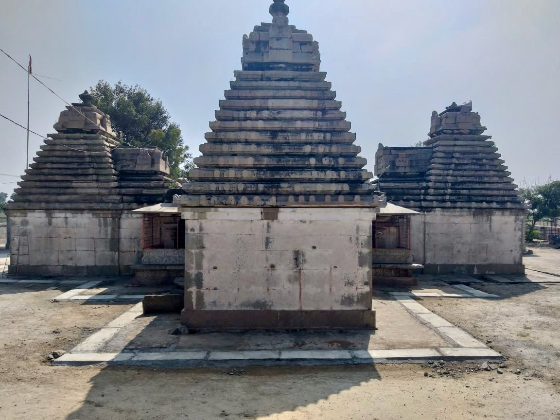 A square stone shrine rises into a tall stepped pyramid tower. Two similar stepped towers stand on either side behind it, under a hazy sky.