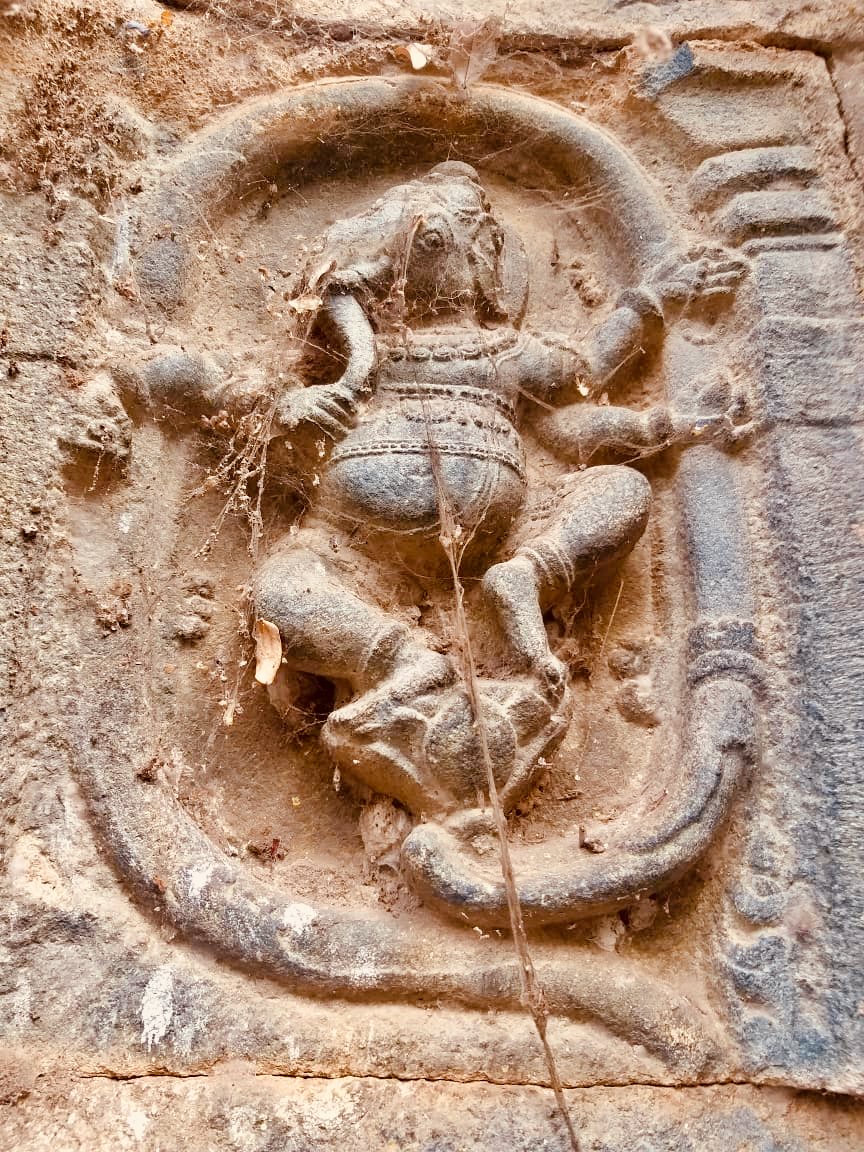 A weathered relief of the elephant-headed god Ganesha dancing inside an oval frame, with his many arms raised.