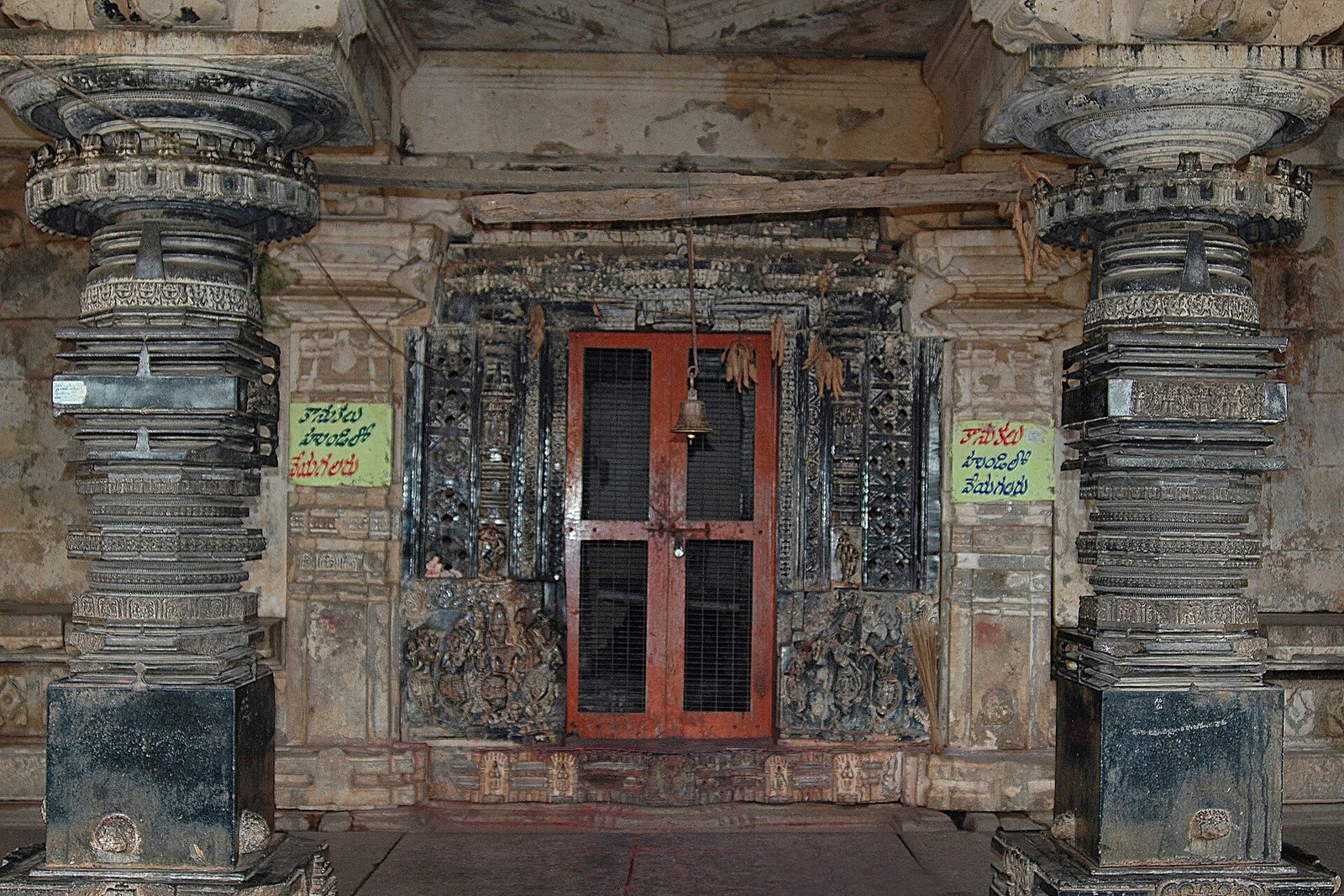 A shrine doorway with carved jambs and perforated screens, flanked by two lathe-turned black stone pillars with ringed and carved bands