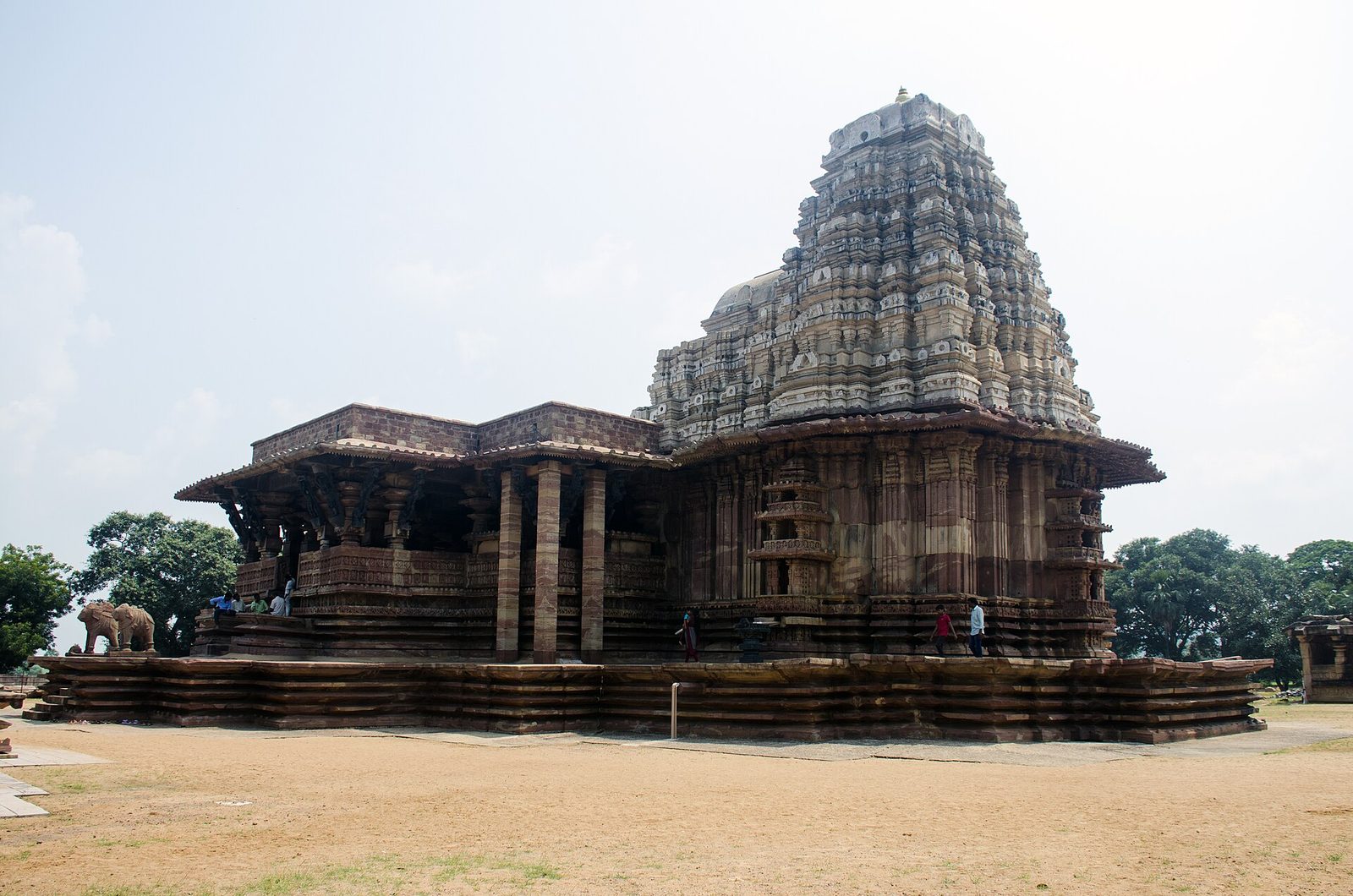 Ramappa Temple under a pale sky: the tall tiered vimana at right and the pillared mandapa at left on a wide stepped platform, with a bare earth courtyard in the foreground