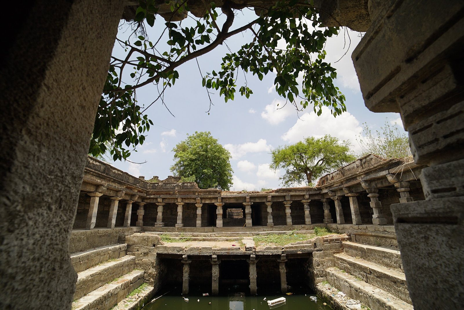 Inside a deep square stepwell: rows of stone pillars carry galleries on several levels, and stone steps lead down to water at the bottom.